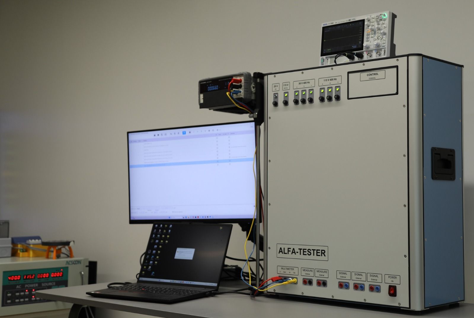 The ALFA-TESTER console with its meter and oscilloscope, a monitor showing a test program, and a laptop